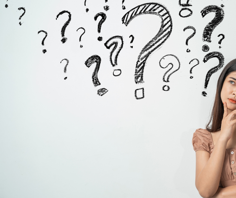 white wall with several question marks written across the top and young lady with dark brown hair and tan shirt on right looking very thoughtful with hand to face as if pondering questions.