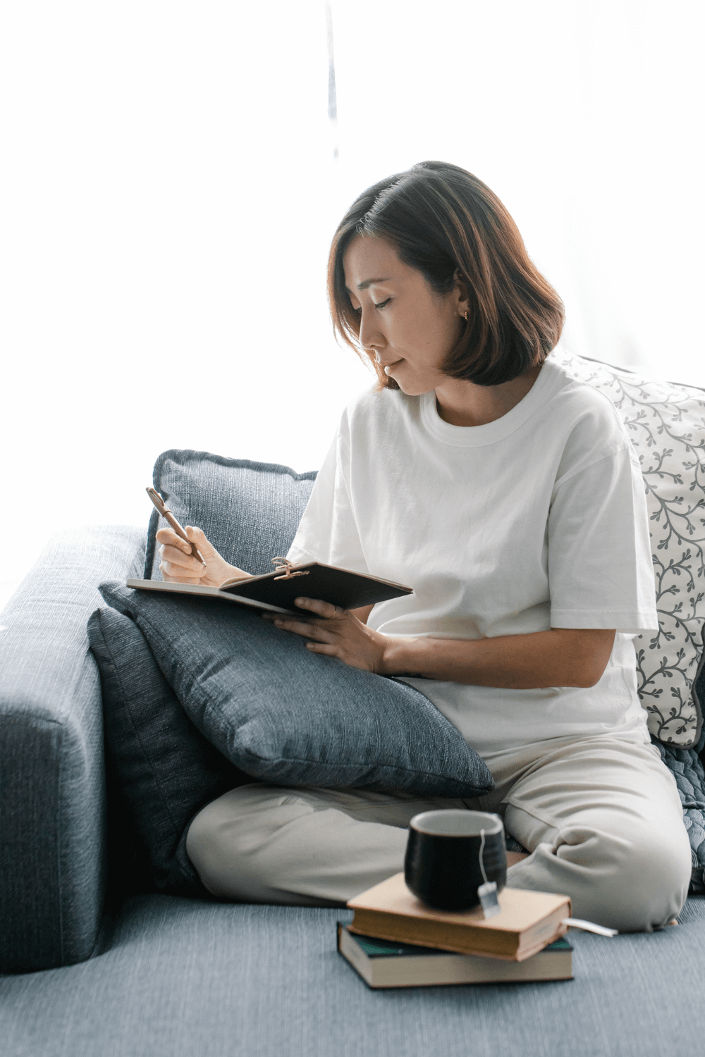 woman journaling at night with a cup of tea, creating a bedtime routine for wellness