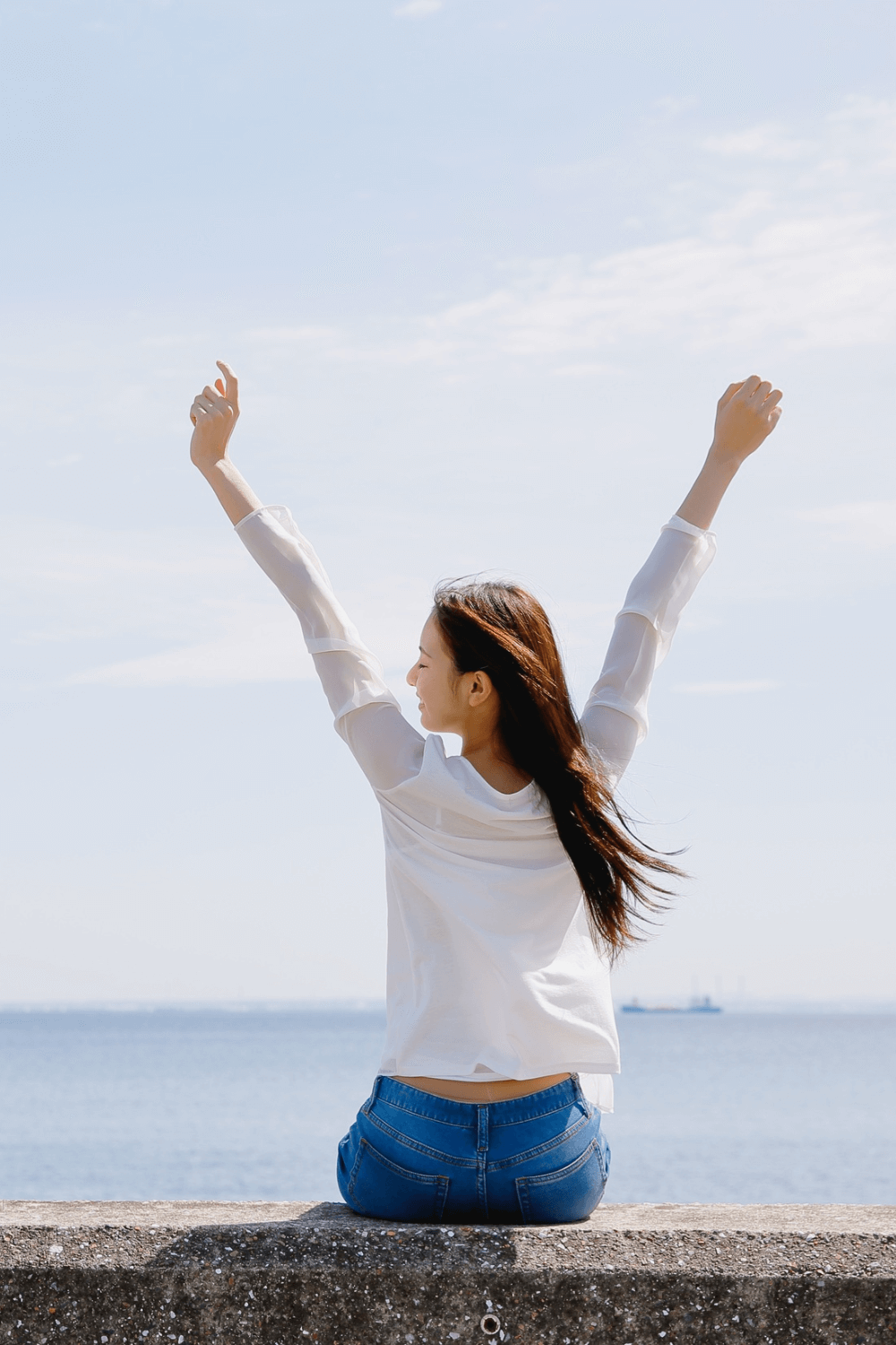  Woman outdoors by the sea with arms raised, symbolizing emotional wellness and vibrant energy.