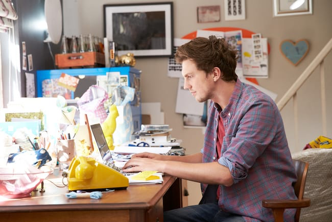 A man with a very cluttered desk in a home office tries to work