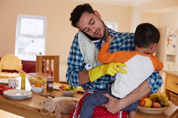 A father holds young son while trying to be productive working from home