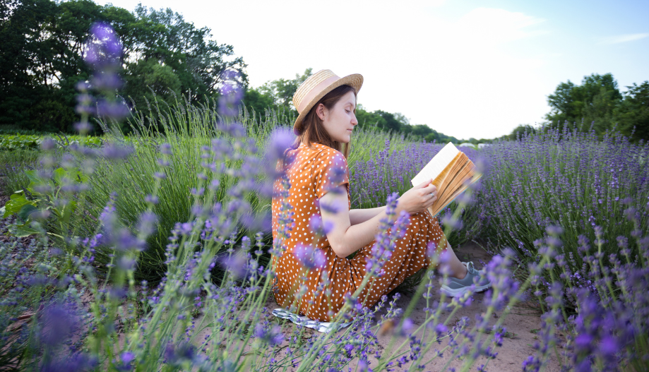 Woman wearing hat sitting in a lavender field reading a journal
