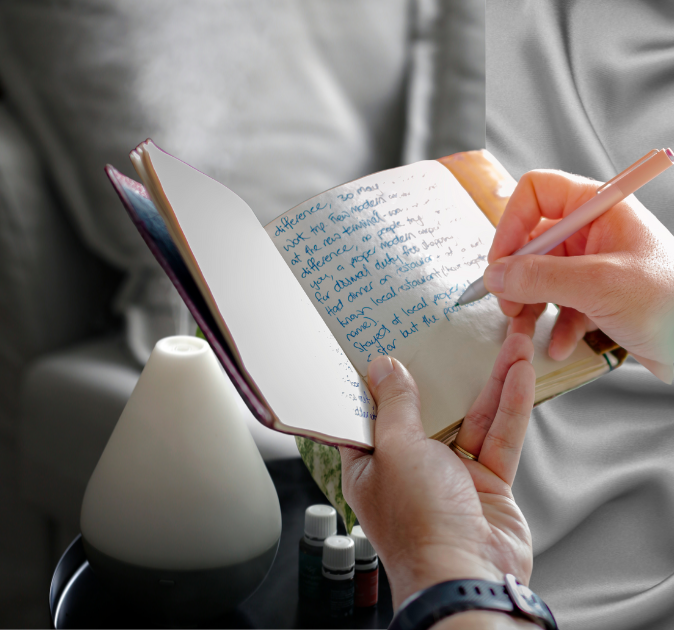 hand holding journal while the other writes, diffuser and young living essential oils on coffee table