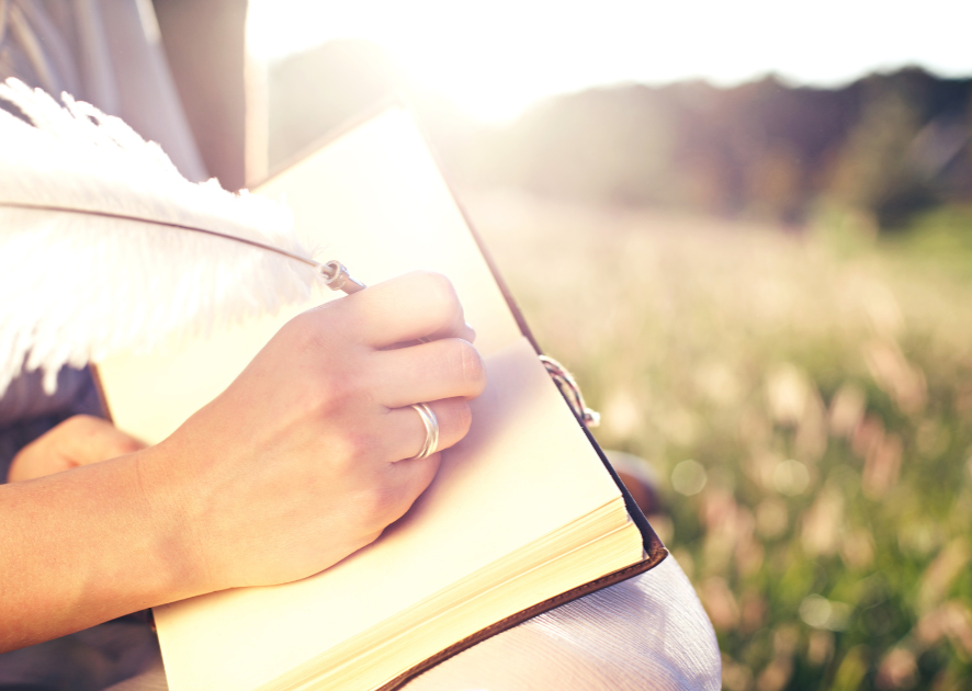 a hand writing in a journal on their knee sitting in nature