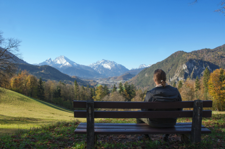man sitting on a bench journaling while facing a mountain valley and mountains and trees in the background