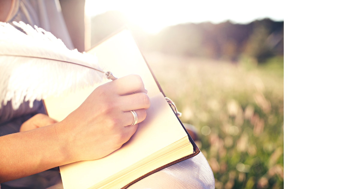 hand on journal holding quill pen writing while in nature