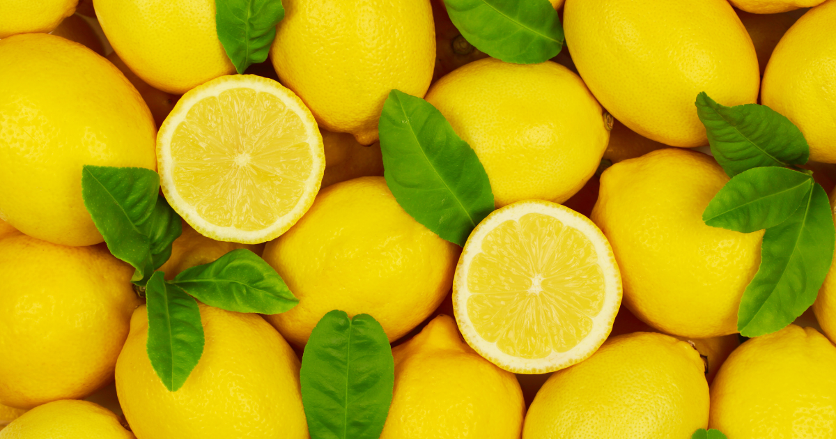 lemons sitting tightly together with a few green leaves and two lemons sliced open
