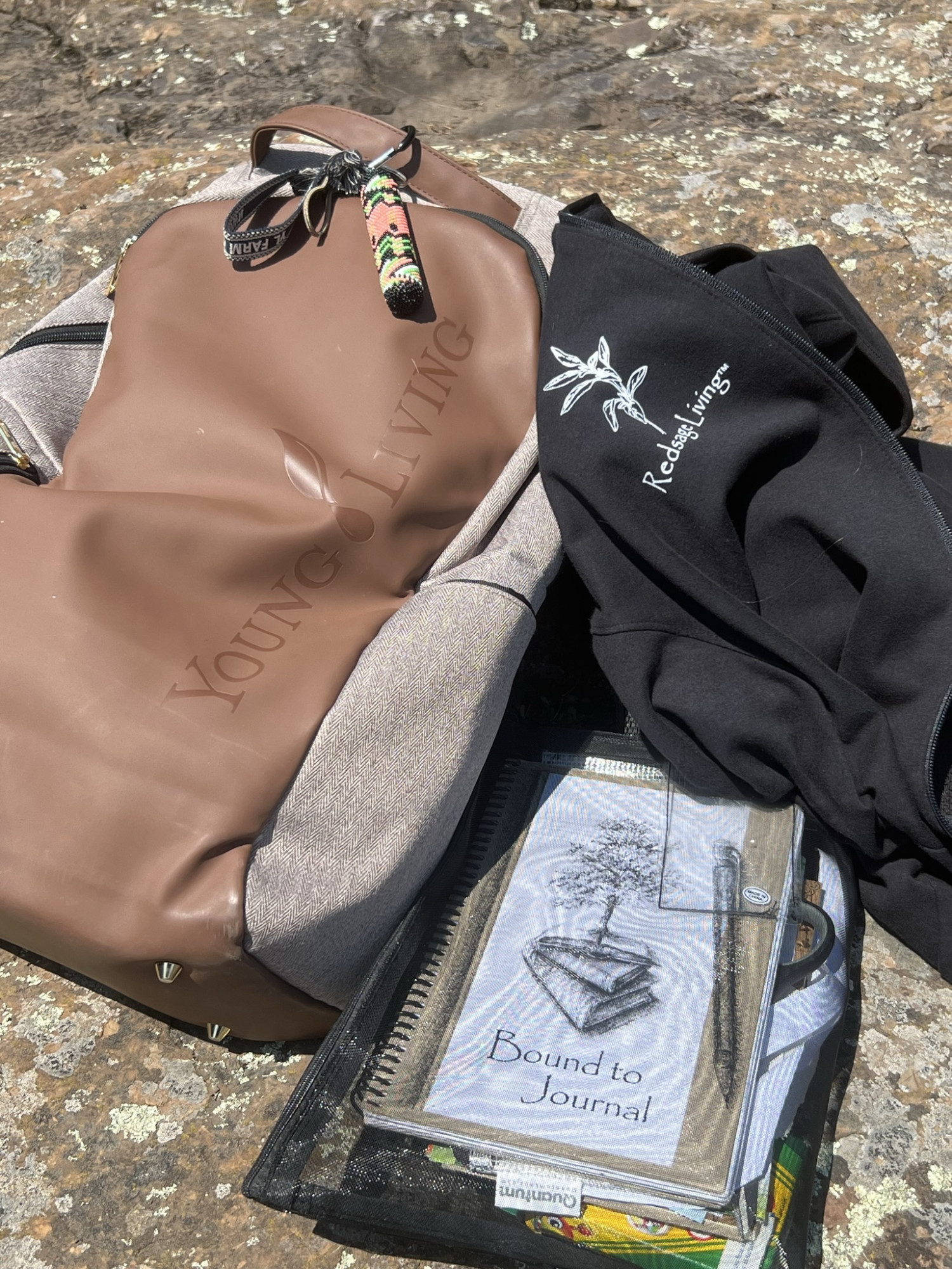 Backpack, journals and journal supplies in a mesh bag, and Redsage Living jacket sitting on rock on Lake Superior.