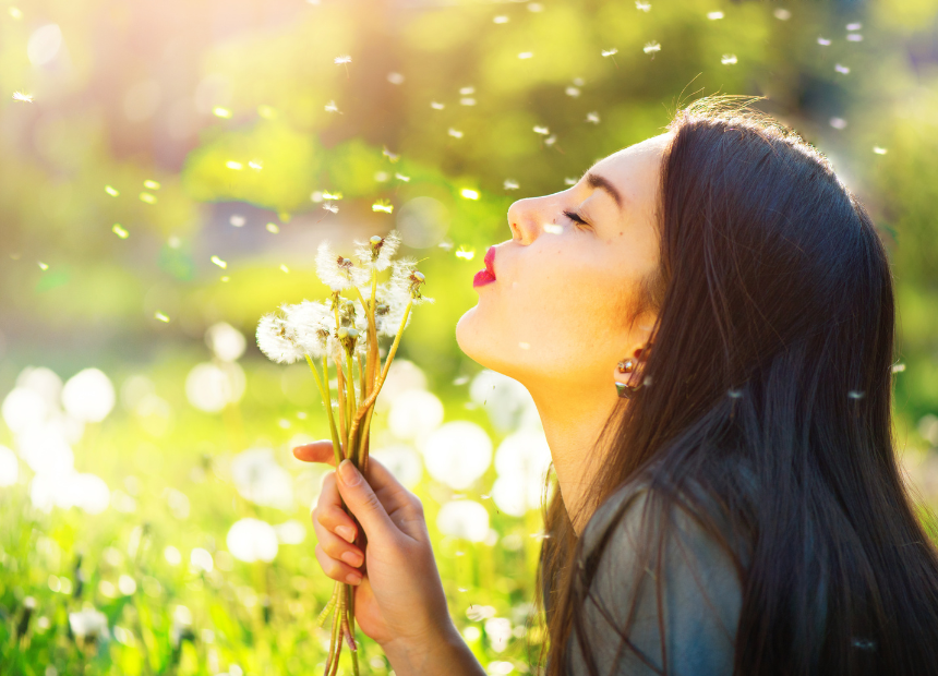 Woman outdoors blowing on a handfull of weeds sending plant particles in the air