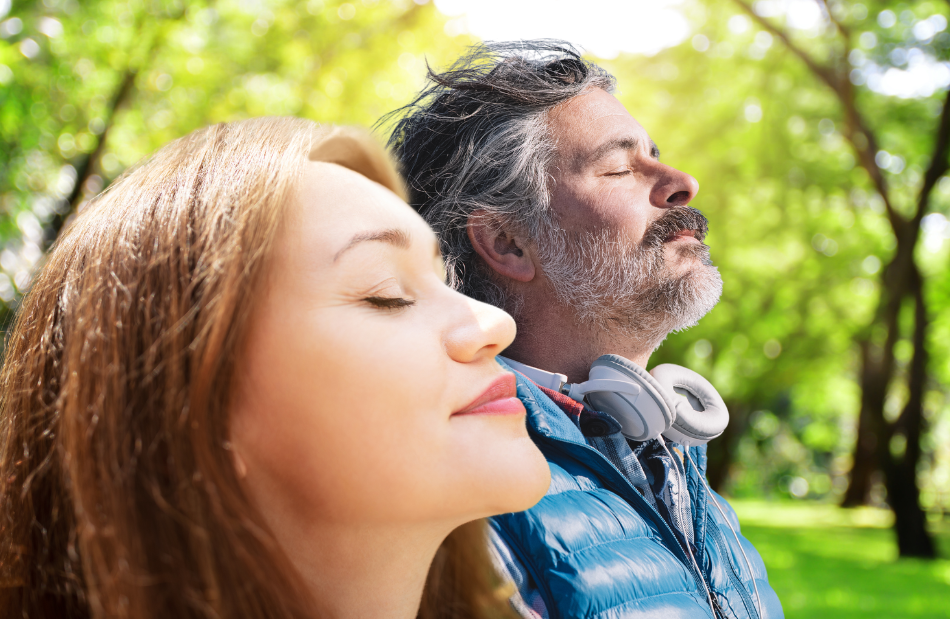 Man and woman out in nature calmly breathing in the air with heads tipped up.