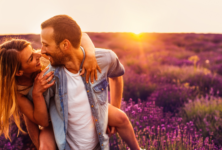 smiling couple man giving woman a piggy back ride in a field of lavender