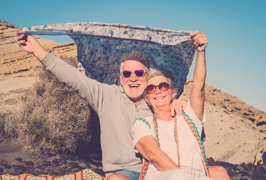 laughing couple in sunglasses on the beach with a cloth held over them