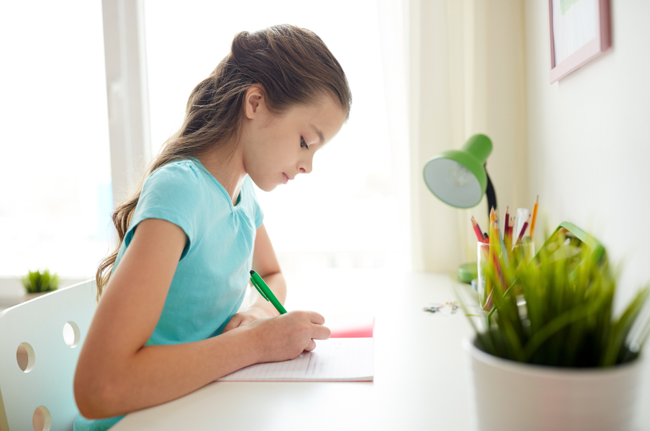 young lady with long hair sitting at a desk writing in her journal