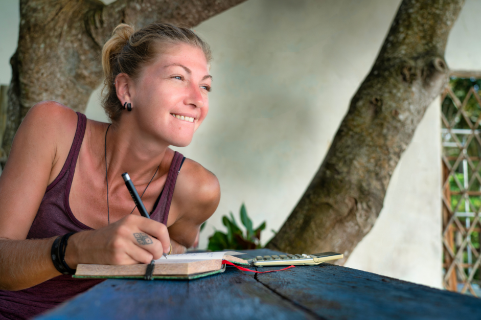 woman smiling like she has a wonderful thought while journaling outside image for post Why Take an Introductory Class for Journaling? 