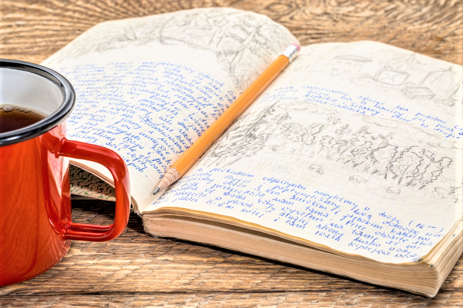 Journal open showing writing and drawing, pencil in spine ditch, and beverage in bright orange cup