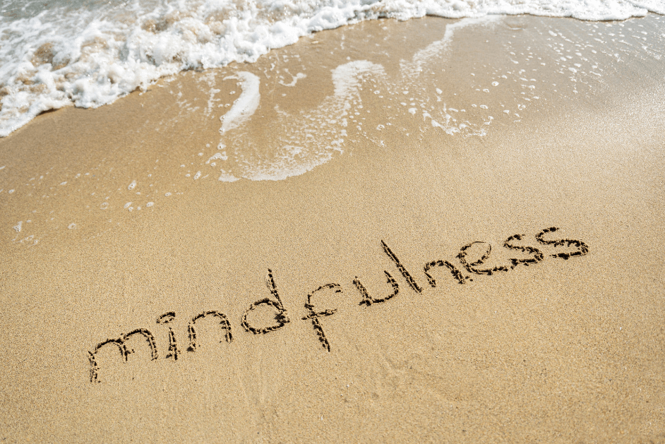 Mindfulness written in the sand on the beach near the water for post titled Journal Prompts to Unlock Creativity, Clarity, and Focus!