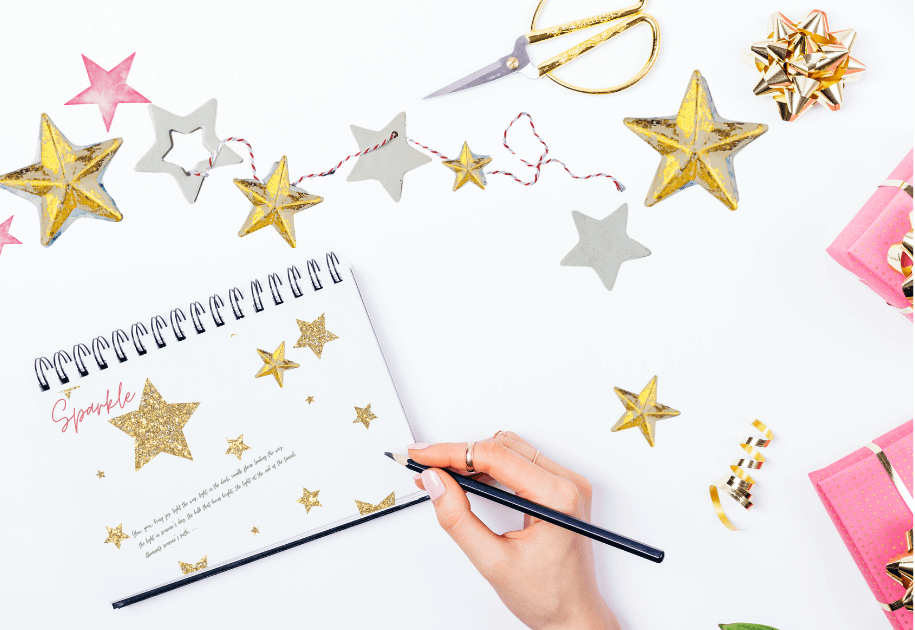 Hand writing in journal with gold stars  and pink wrapped packages for post titled 5 ideas for Using your Journal to preserve the essence of the season! and 