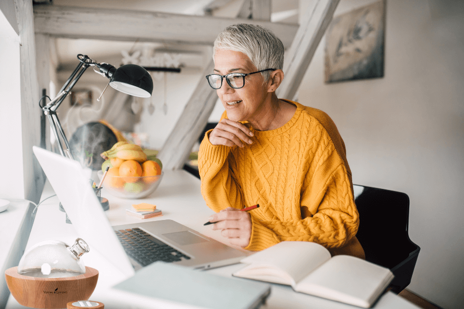 woman sitting at her desk in front of a computer wearing a bright saphron sweater with aria diffuser running for post titled 5 reasons to diffuse essential oils every day!