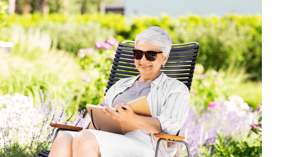 older woman sitting outside near a garden in a lawn chair with her journal for post titled Top 5 Reasons for Creating a Garden Journal