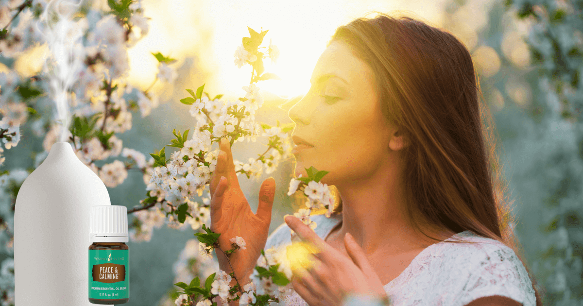 Woman smelling tree blossoms with the glow of sun blurring out part of her image and a diffuser and Young Living essential oil are superimposed on the left side of the image for post titled Spring Aromatherapy: Refreshing Diffuser Recipes