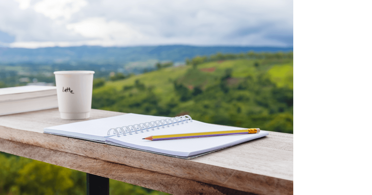 a journal sitting open on a balcony railing, a pencil on the journal, a coffee cup and book nearby, with a beautiful mountainous view in the distance for post titled  7 Hidden Journaling Hurdles: Uncovering Why Many Hesitate to Start 