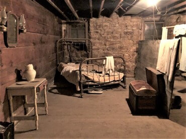 A Short term bed area next to a trunk, washing table with pitcher, mirror and laundry area for latest post called Underground History, Mystery, and Curiosity-Inspired Journaling