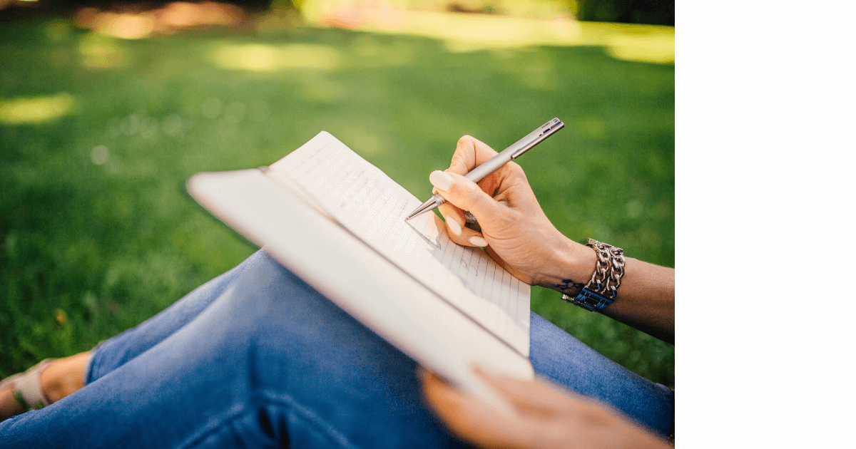 person sitting outside on the ground journaling for post titled Embrace Hygge with Journaling and Essential Oils