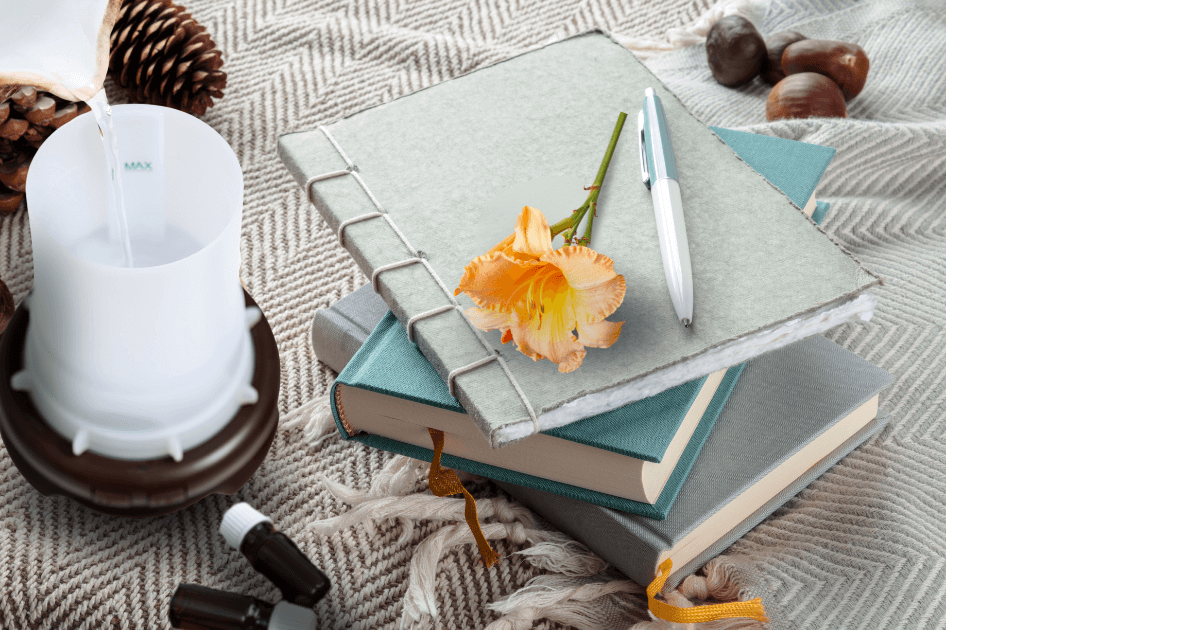 Open diffuser, essential oils, a stack of journals, pen, and day lilly sitting on a woven wrap for post titled Embrace Hygge with Journaling and Essential Oils