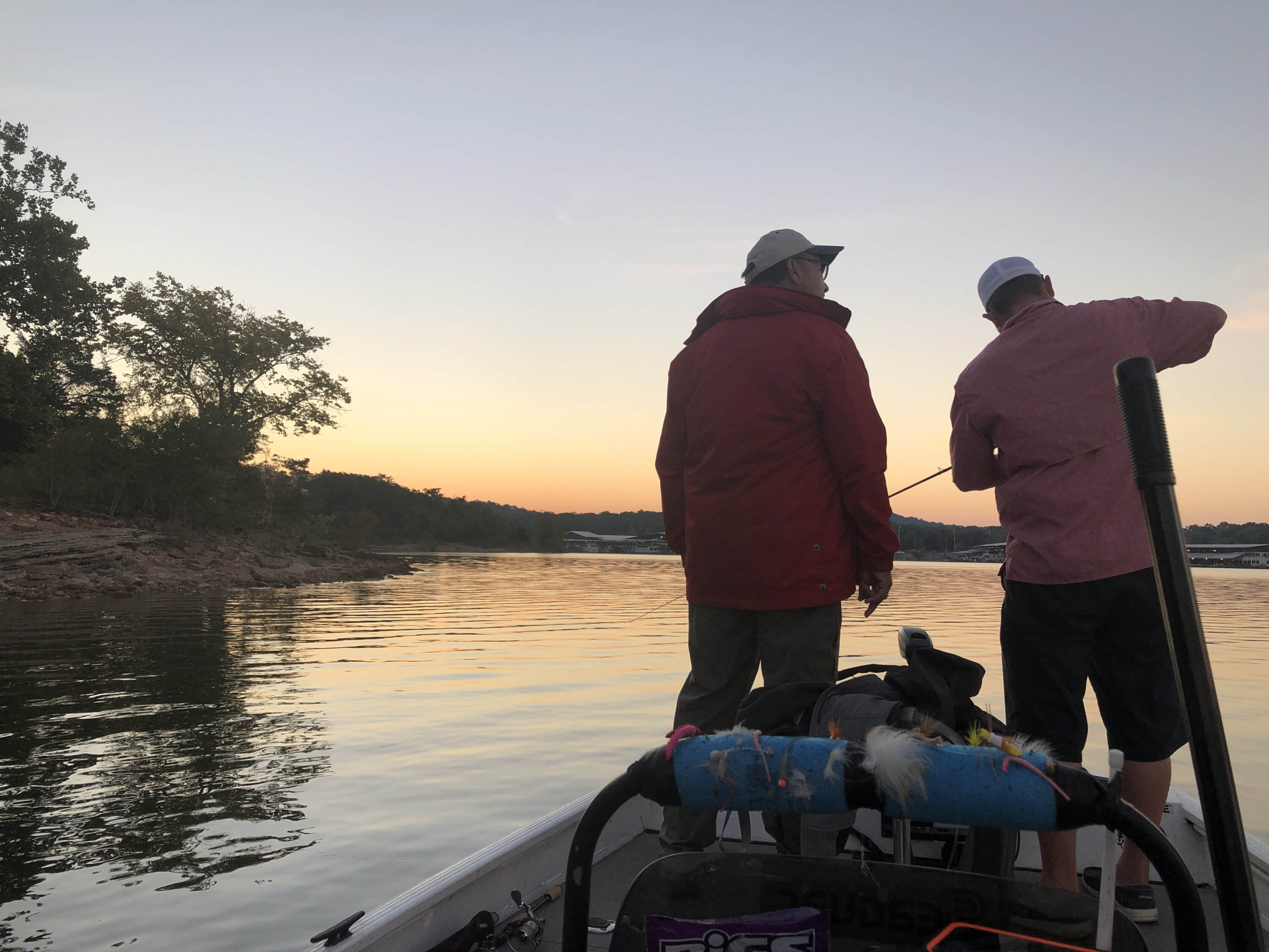 Allen standing on a boat at sunrise next to our guide who's preparing the fishing line for a blog post titled Reeling in the Benefits of a Fishing Journal