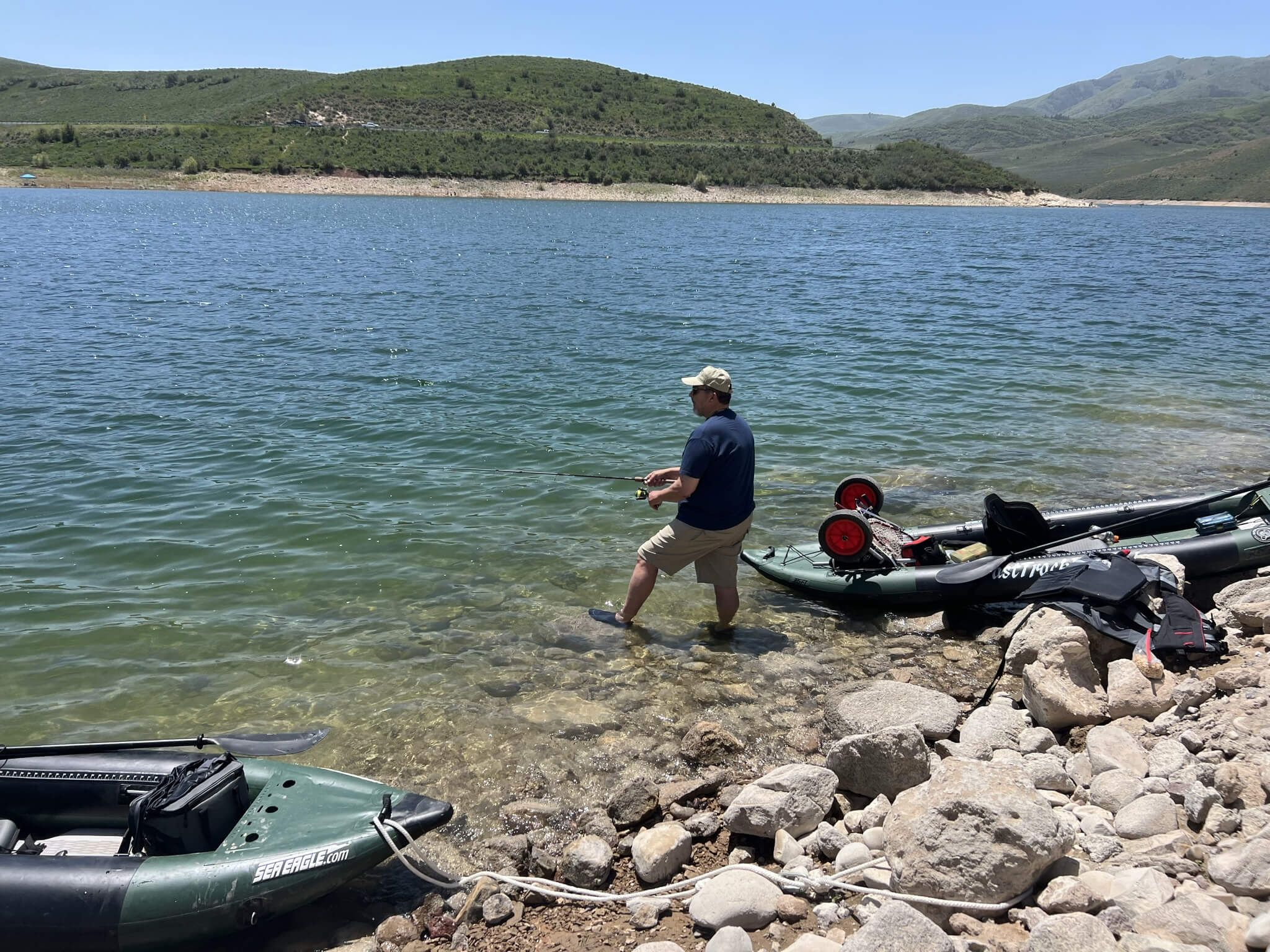 Allen standing in the water at the edge of a lake in Utah casting into the water with two inflateable kayaks on the shore for a blog post titled Reeling in the Benefits of a Fishing Journal