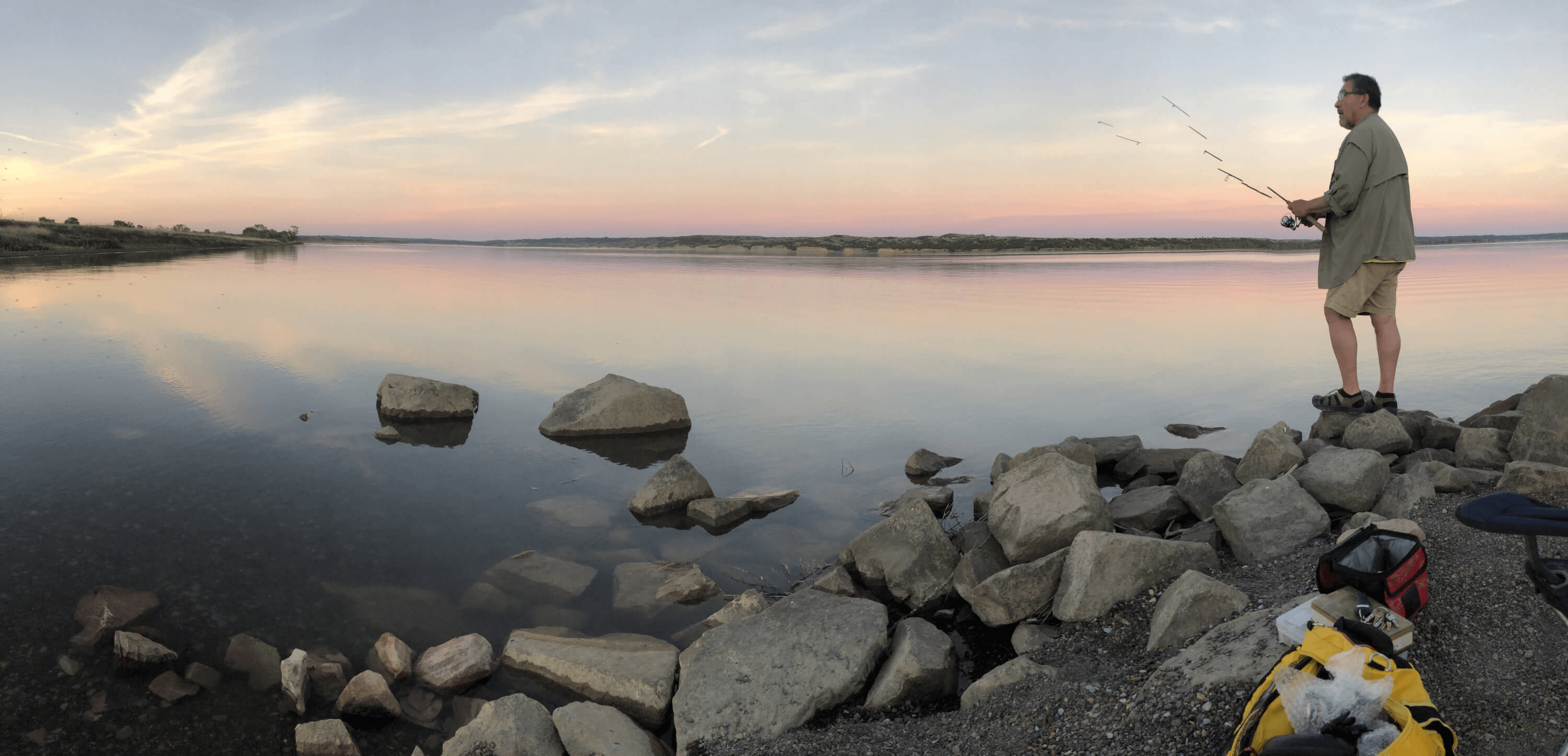 Allen fishing on a rocky shore of a lake and casting into  the water at sunset for a blog post titled Reeling in the Benefits of a Fishing Journal