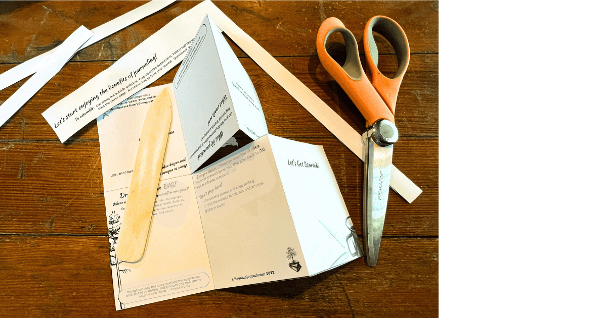 A folded but unassembled one-page journal sitting on a table next to a bone folder, scissors, and the trimmed edges from the download page all on a wooden table for the new blog post titled 4 Reasons to Create a One-Page Journal Today!