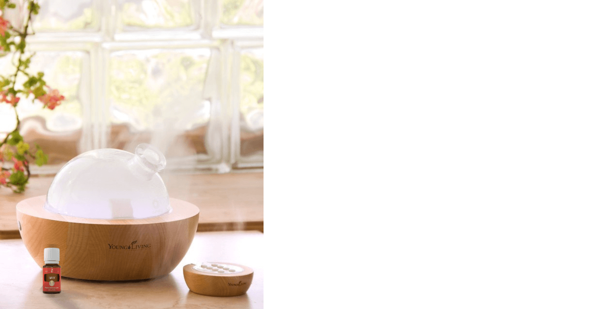 An Aria diffuser near a nature light block window, orange blossoms on a plant, and a bottle of Young Living Raven essential oil for a blog post titled Top 5 Ways We Use Raven™ Essential Oil