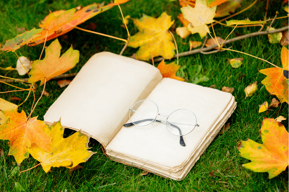  An open journal with a glasses laying in the grass with fall colored leaves sprinkled around  for our Bound to Journal  blog post titled The Art of Forest Bathing, Journaling, and Essential Oils