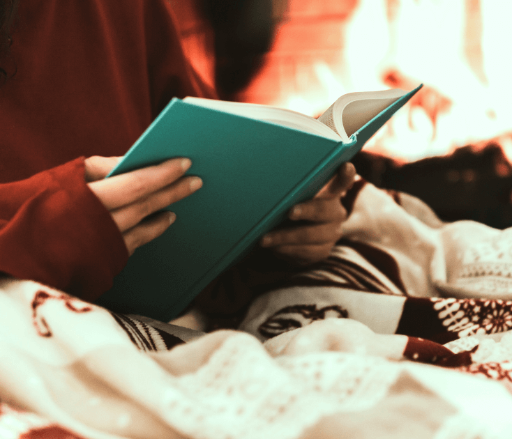 Person sitting crosslegged, wrapped up in a cozy blanket, working in their journal  for a blog post titled Winter Diffuser Recipes for Clarity, Inspiration, and Cozy Productivity