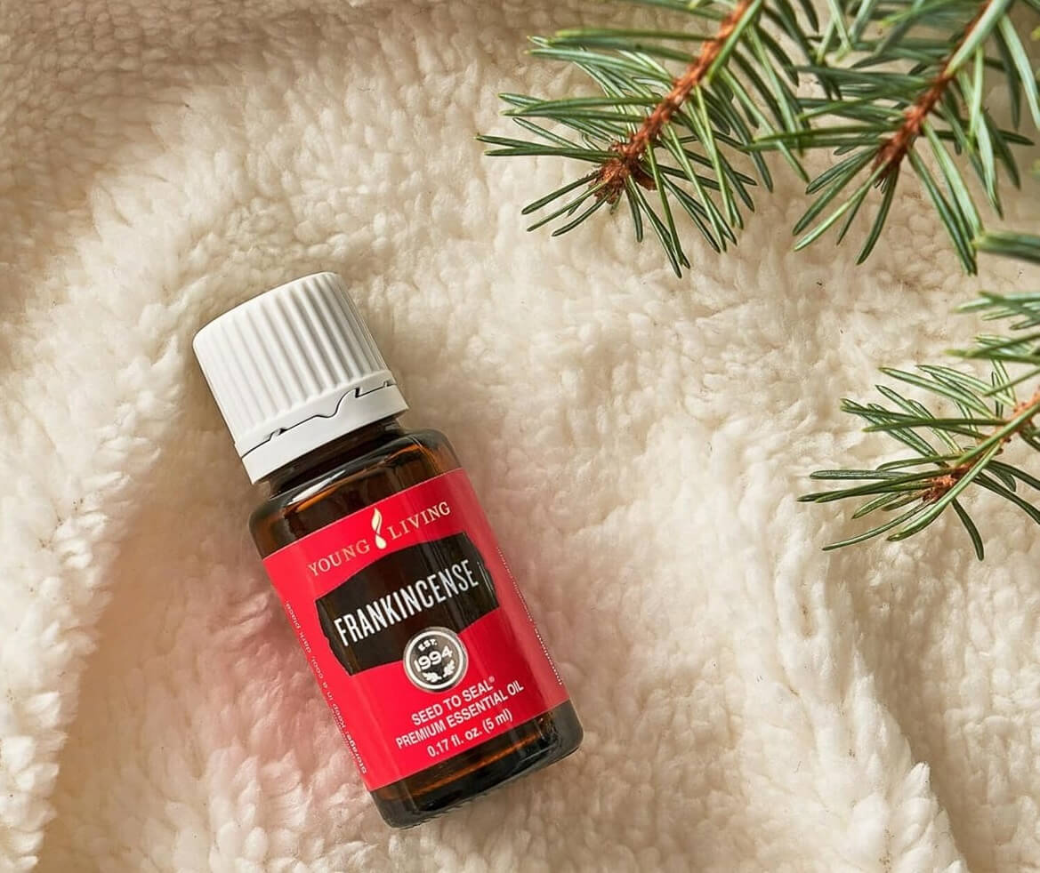  A bottle of young living essential oil frankincense laying on a white furry blanket and an evergreen branch along side for a blog post titled Ancient Oils: The Perfect Companion for Holiday Journaling