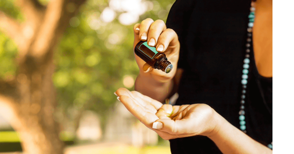  A person dropping young living essential oils in to the palm of her hand with trees abd bright sunny park like setting behind her for  for our Bound to Journal blog post titled Traveling with Essential Oils: Your Ultimate Guide to Serenity on the Go