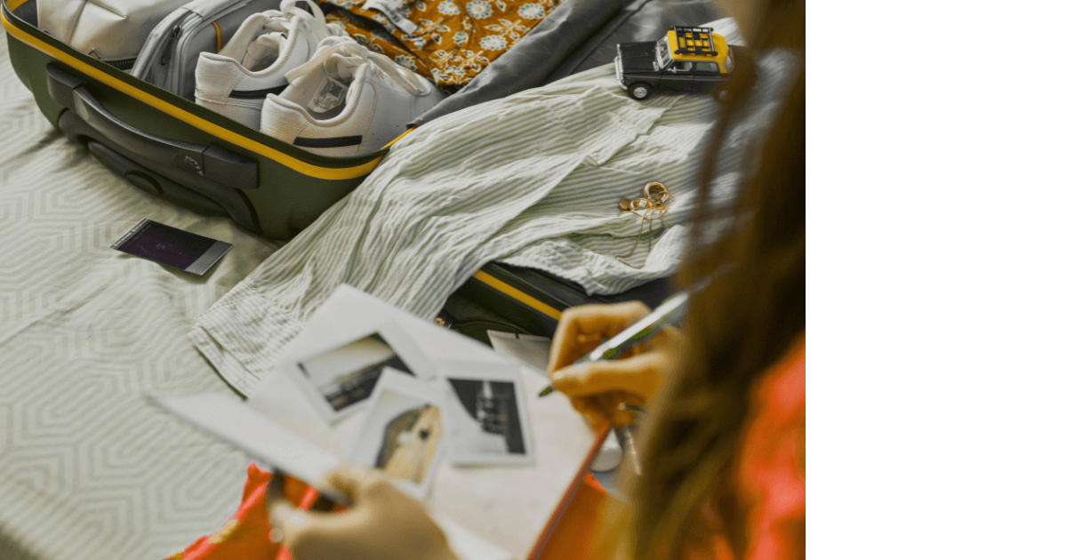  A person sitting on a bed with an open journal, photos, and a pen ready to write, an open suitcase in the process of being packed for a Bound to Journal blog post titled Packing Light: Your Journal as an Essential Travel Companion