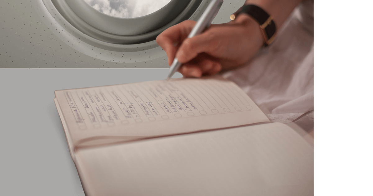  A person sitting by the window on an airplane using the dropdown table to write in her journal for a Bound to Journal blog post titled Packing Light: Your Journal as an Essential Travel Companion