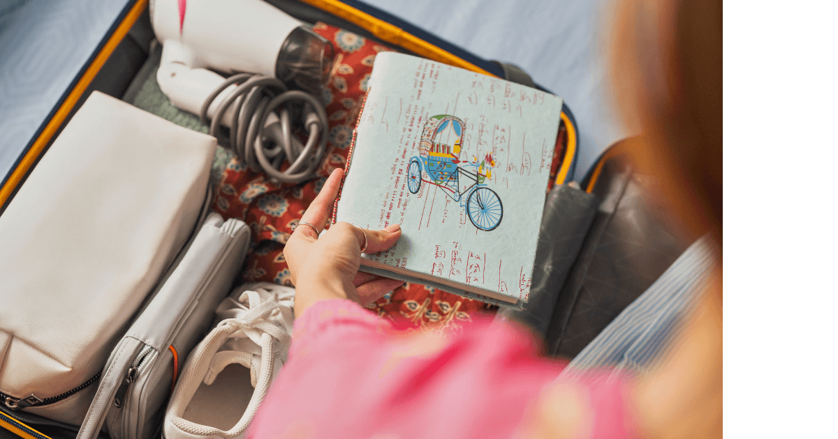  Someone about to put a journal with a decorative cover into their open suitcase for a Bound to Journal blog post titled Packing Light: Your Journal as an Essential Travel Companion