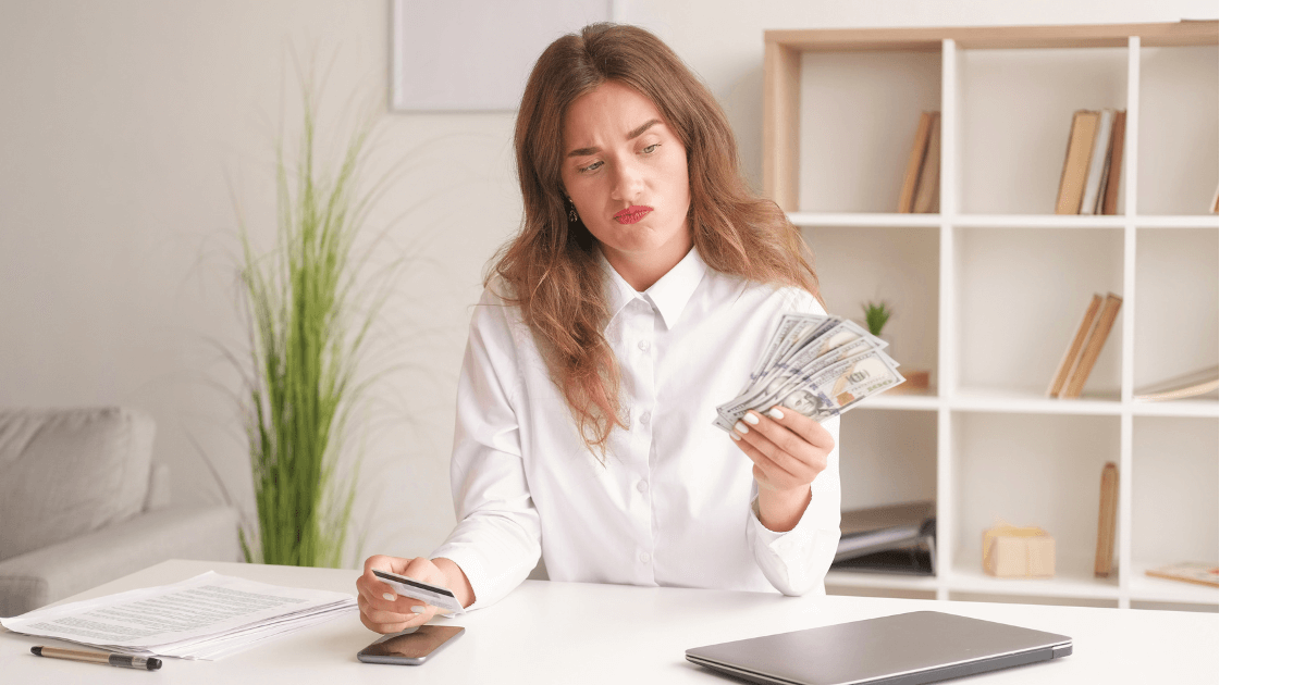  A woman sitting at a desk in a home office with a questioning look on her face.  In one hand she holds a stack of money and the other a credit card for a Bound to Journal blog post titled Navigating the Essential Oil Labyrinth: Empowering Yourself as a Confident Consumer