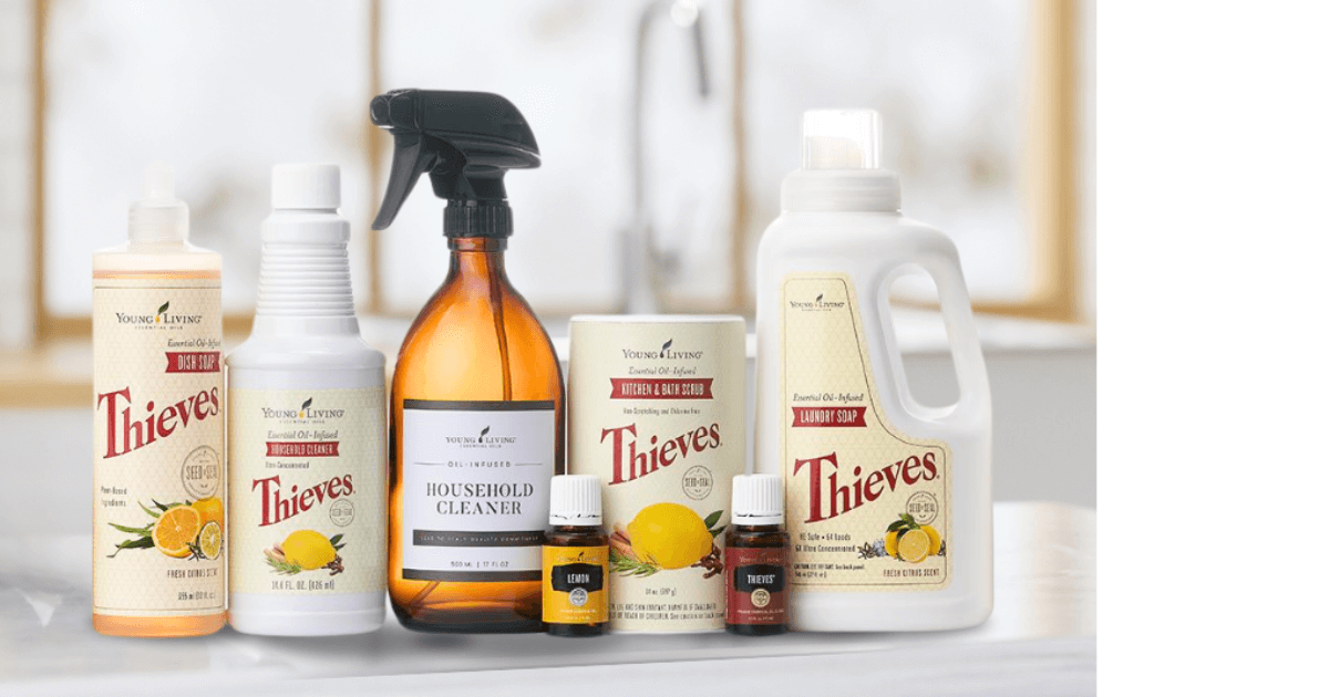 Bottles of Thieves dish soap, household cleaner, scrubbing powder, and laundry soap plus a spray bottle labeled for thieves household cleaner and a bottle of lemon essential oil and a bottle of thieves essential oil on a bathroom counter top in a brightly lit white room for a Bound to Journal Blog post titled Thieves Household Cleaner: Your Year-Round Solution for Safe, Natural Cleaning