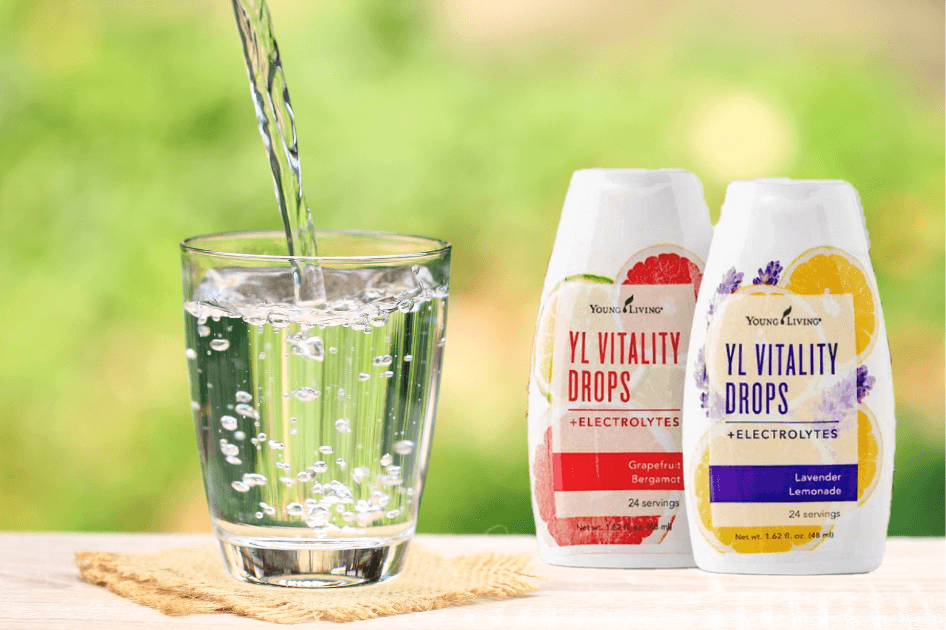 Fresh water pouring into a glass sitting next to two bottles of Young Living's Vitality Drops  for a Bound to Journal blog post titled Add Vitality: Essential Oils to Make Hydration and Summer Journaling More Fun