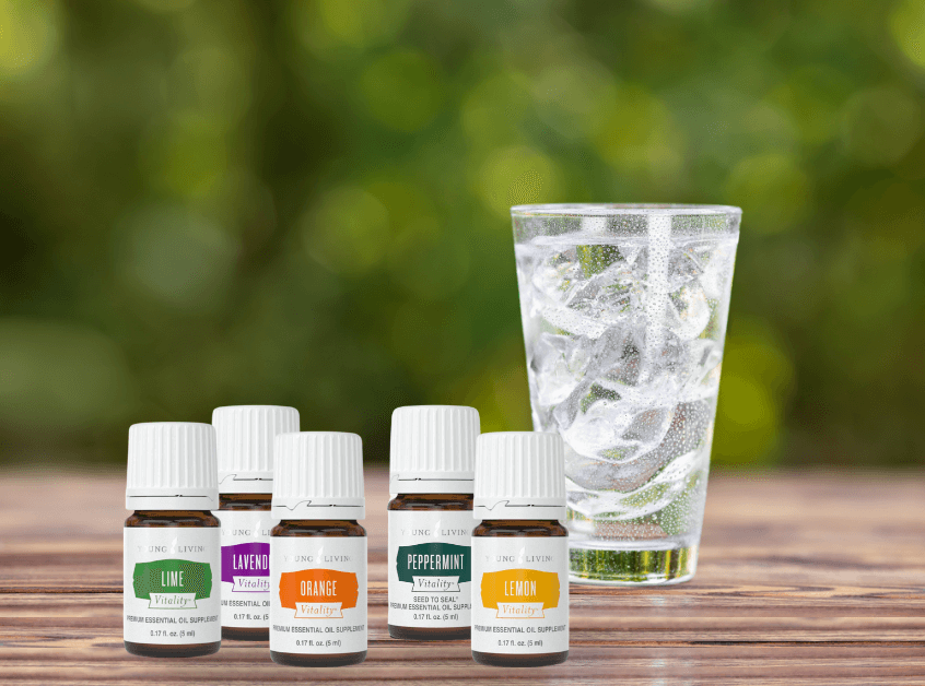  Five bottles of Young Living's vitality essential oils next to a glass sitting on a wooden outdoor table is filled with water and ice cubes  for a Bound to Journal blog post titled Add Vitality: Essential Oils to Make Hydration and Summer Journaling More Fun