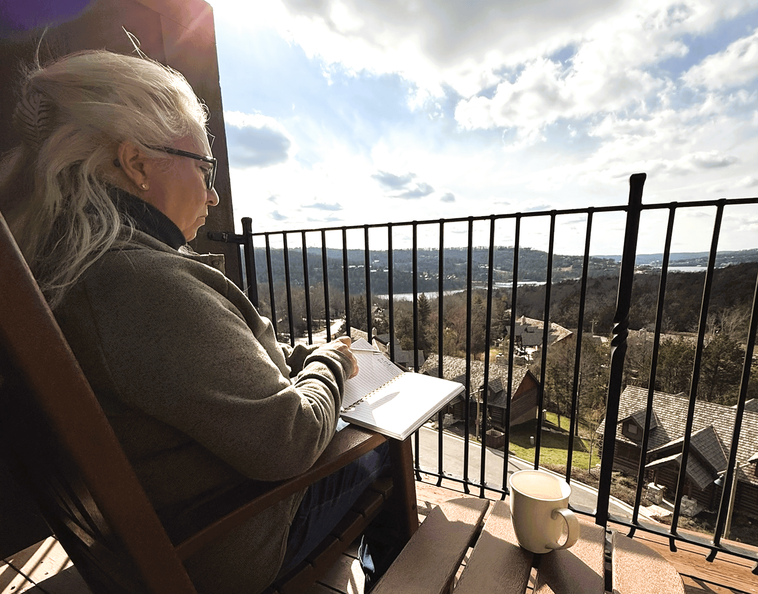 Me journaling on a balcony deck overlooking the Ozark mountains with a cup of coffee next to me for a Bound to Journal blog post titled Amplifying the Benefits of Journaling: Engaging Your Senses