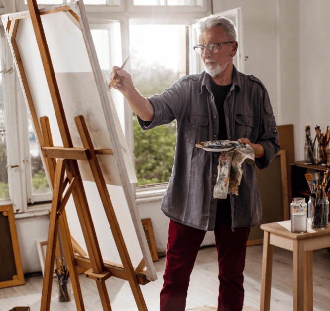  A man holding a palette, brush, and paint rag  standing in front of a large canvas in an art studio  for a Bound to Journal blog post titled Reignite Your Passions: Journaling & Creativity for Aging Gracefully