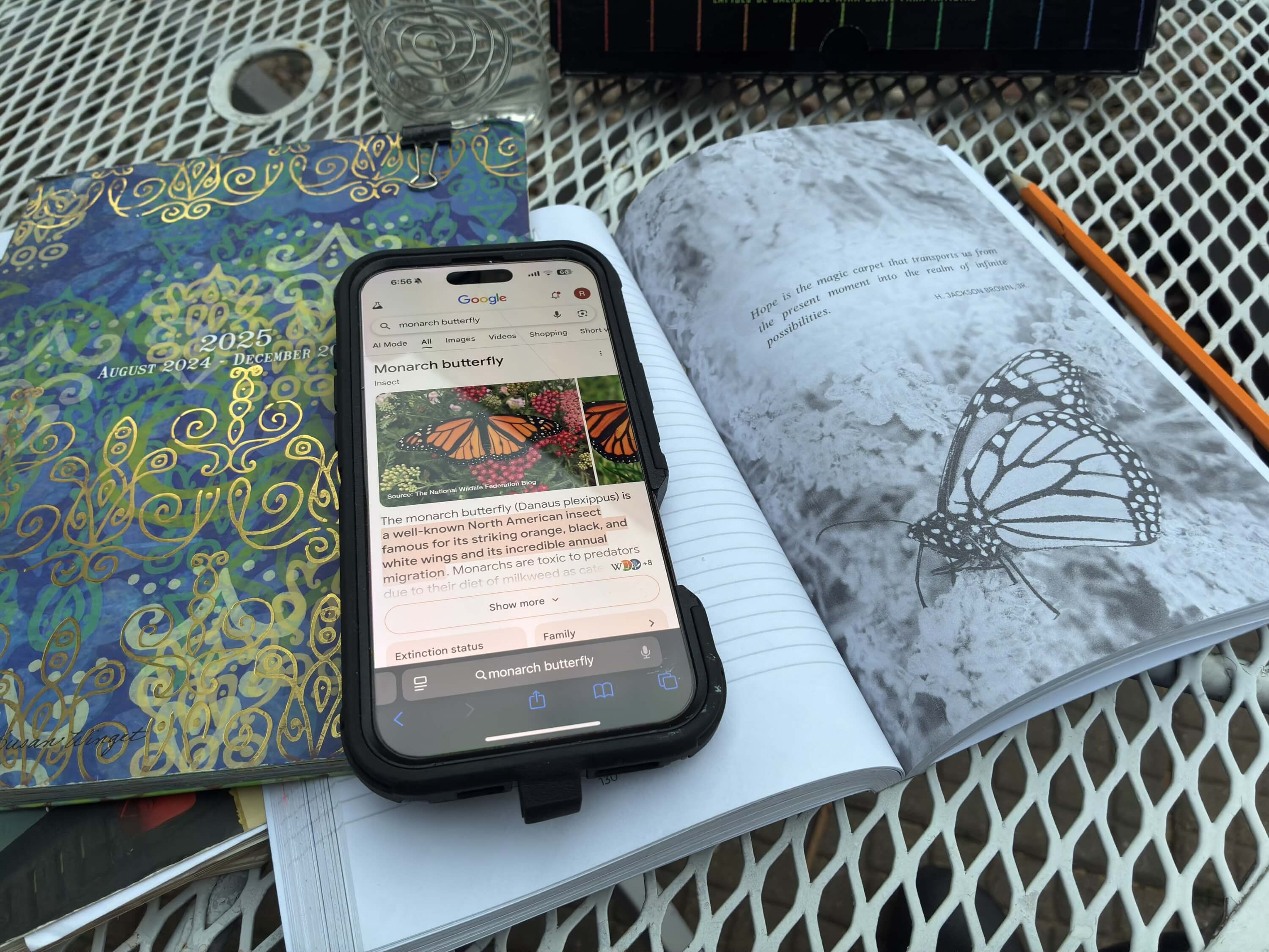  An iPhone open to a butterfly image all sitting on an outdoor table Colored pencil work on a pause page in "Find Your Voice, Live Your Purpose" guided journal for a Bound to Journal  post called The Quiet Power of Pausing: A Guided Journal Tip