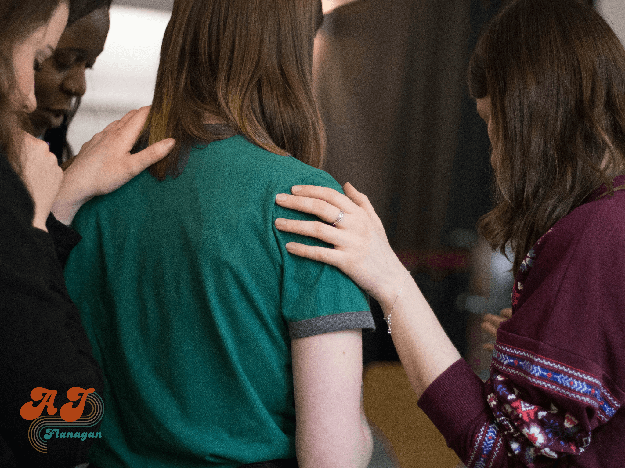 Four people placing hands on each other's shoulders in a supportive manner