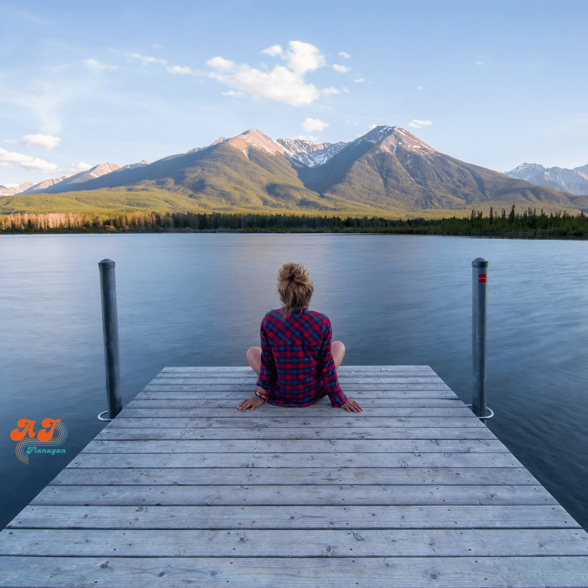 Calming, reflective photo of a woman sitting on a dock by a mountain lake