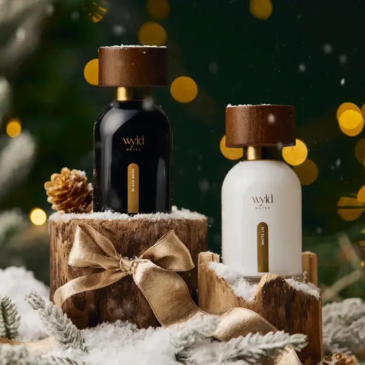  Wyld Notes™ fragrance duo — curated modern botanical scents in black and white bottles; winter holiday styling with snow and pine.